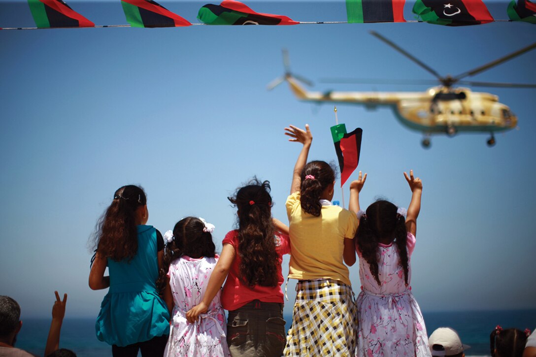 Girls wave and flash victory signs at passing helicopter during military parade in western city of Zawiya, Libya, held to mark anniversary of uprising last year that cleared way for anti-Qadhafi forces’ march on Tripoli, June 11, 2012 (United Nations/Iason Foounten)