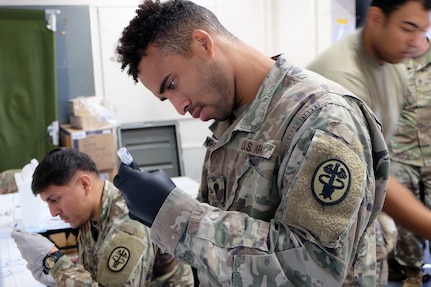 Spc. Rashawn Shepperd (foreground) and Sgt. Oscar Caro, draw syringes that will be used to administer measles, mumps and rubella syringes and chickenpox syringes to Afghan evacuees