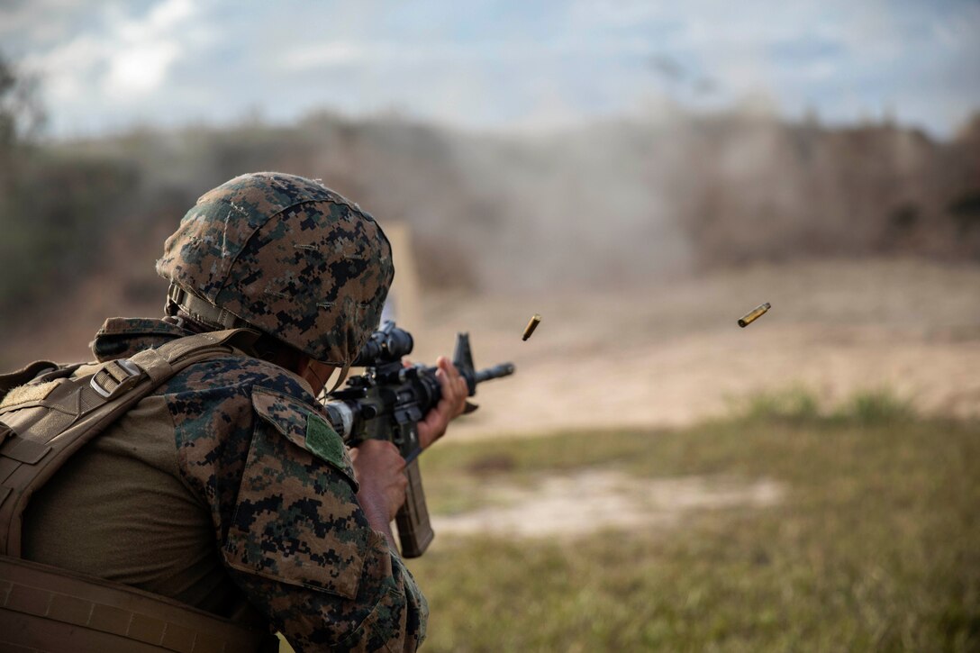 A Marine fires a weapon in a field.