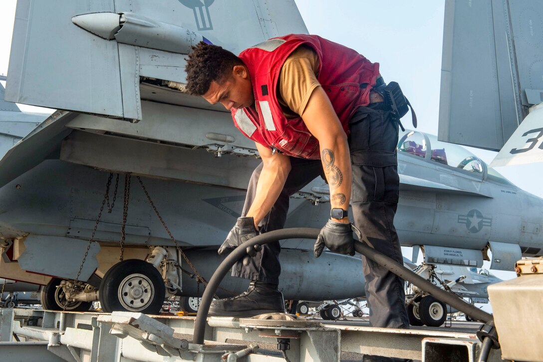 A sailor stows a power cable on a ship.