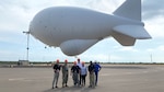 a group of people stand in front of an aerostat balloon