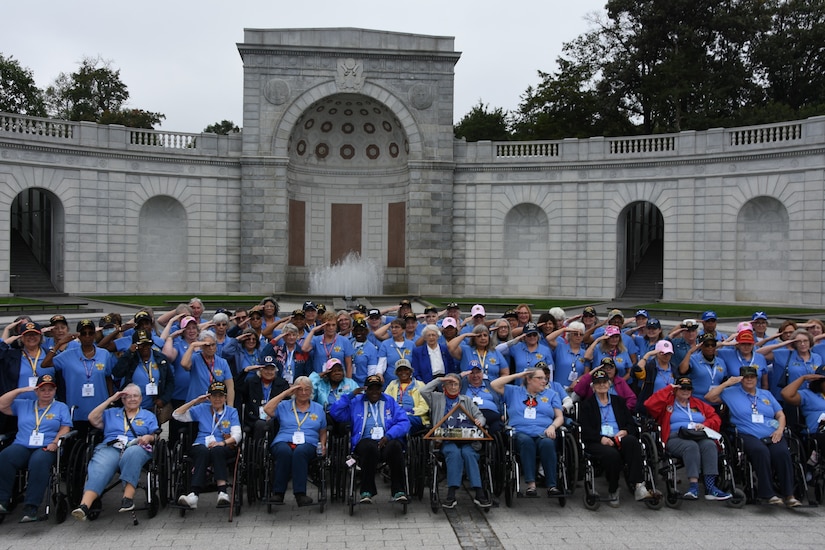 A large group of elderly women, many in wheelchairs, salute.