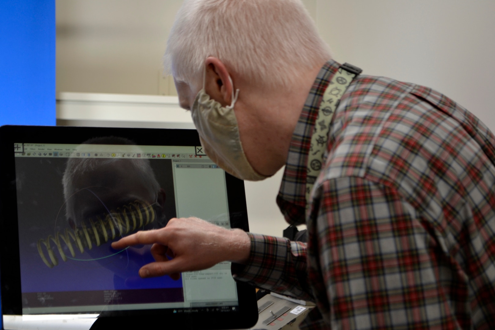 A man in a checkered shirt touches a computer screen to manipulate the 3D image of a spring.