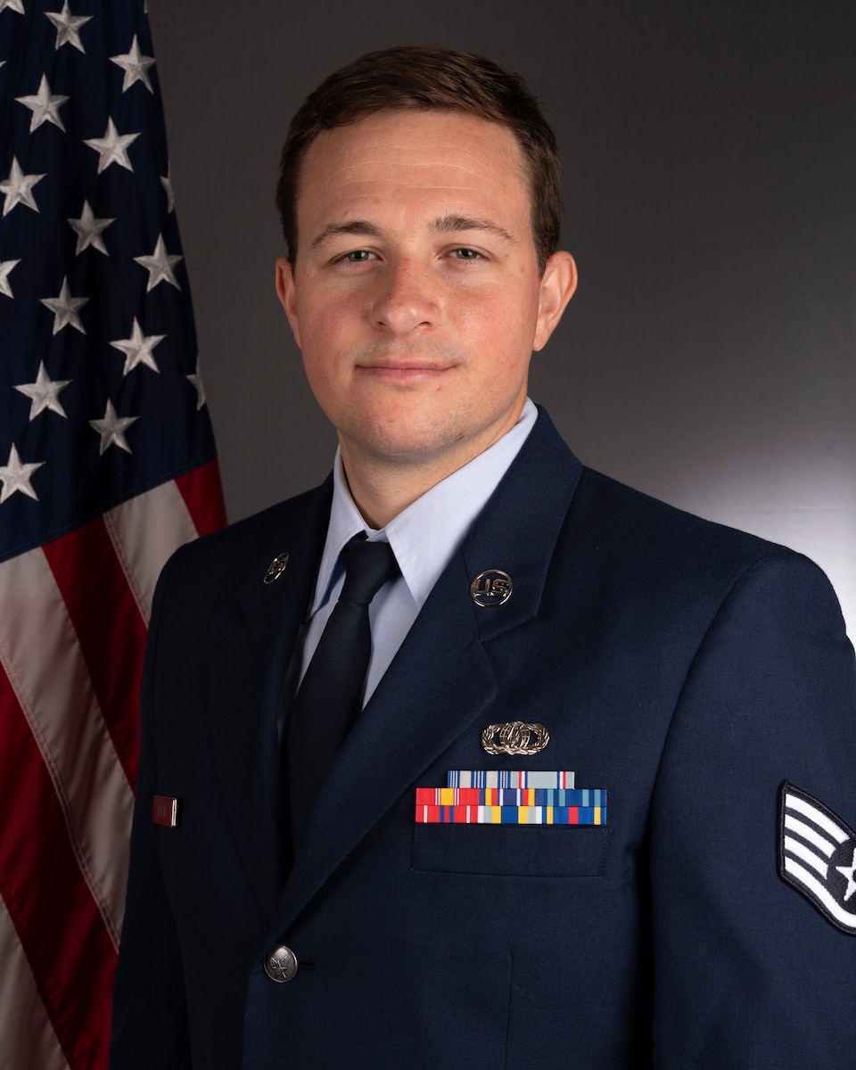 Official photo of SSgt Brian Logan, euphonium with Heritage Brass and the Concert Band, two of six ensembles in the Air Force Heritage of America Band, Langley AFB, VA.  SSgt Logan is wearing blue service dress in front of an American flag.