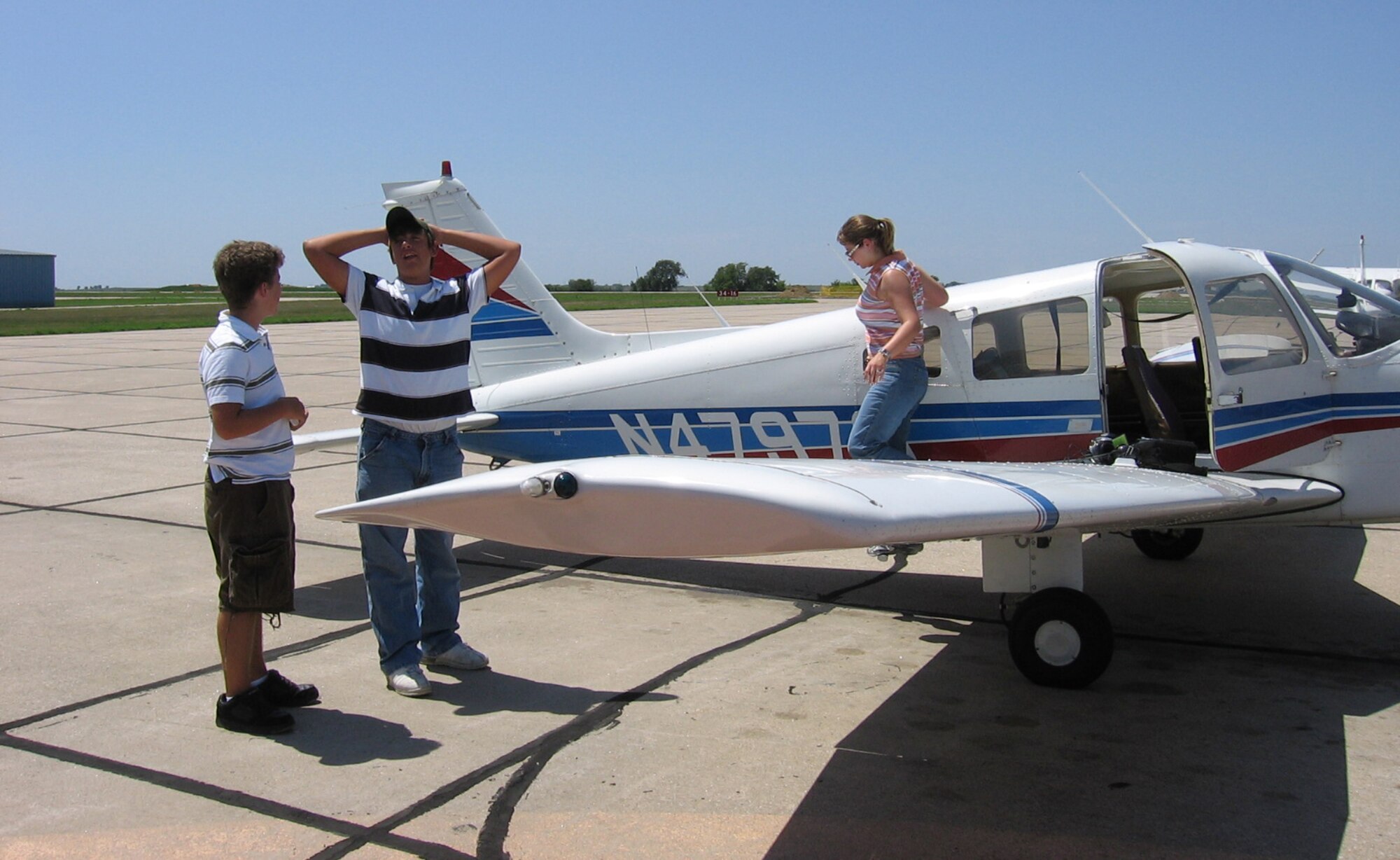 Three people standing outside of a small airplane.