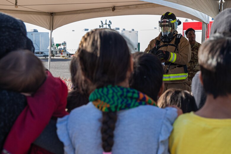 Airman 1st Class Justice Smith, Task Force-Holloman firefighter deployed from Seymour Johnson Air Force Base, North Carolina, demonstrates the proper wear of firefighter gear as well as giving a fire safety class to younger Afghan evacuees on Holloman Air Force Base, New Mexico, Oct. 11, 2021. The Department of Defense, through U.S. Northern Command, and in support of the Department of Homeland Security, is providing transportation, temporary housing, medical screening, and general support for at least 50,000 Afghan evacuees at suitable facilities, in permanent or temporary structures, as quickly as possible. This initiative provides Afghan personnel essential support at secure locations outside Afghanistan. (U.S. Army photo by Pfc. Anthony Sanchez)