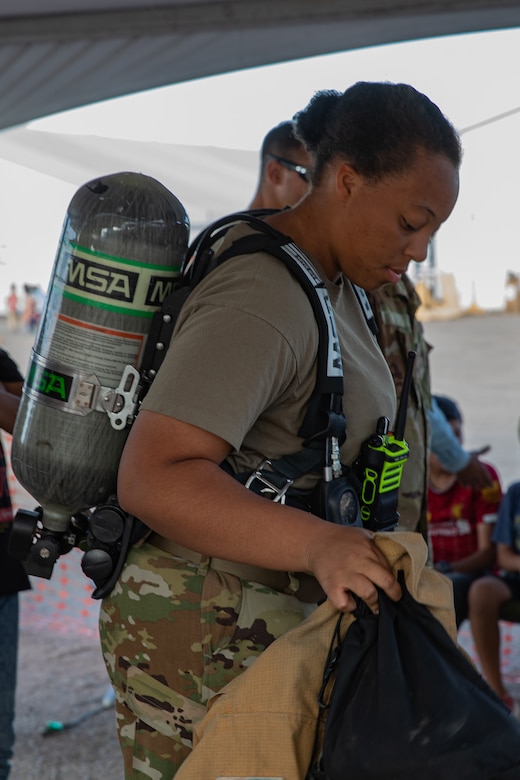 Airman 1st Class Justice Smith, Task Force-Holloman firefighter deployed from Seymour Johnson Air Force Base, North Carolina, demonstrates the proper wear of firefighter gear on Holloman Air Force Base, New Mexico, Oct. 11, 2021. The Department of Defense, through the U.S. Northern Command, and in support of the Department of State and Department of Homeland Security, is providing transportation, temporary housing, medical screening, and general support for at least 50,000 Afghan evacuees at suitable facilities, in permanent or temporary structures, as quickly as possible. This initiative provides Afghan evacuees essential support at secure locations outside Afghanistan. (U.S. Army photo by Spc. Nicholas Goodman)