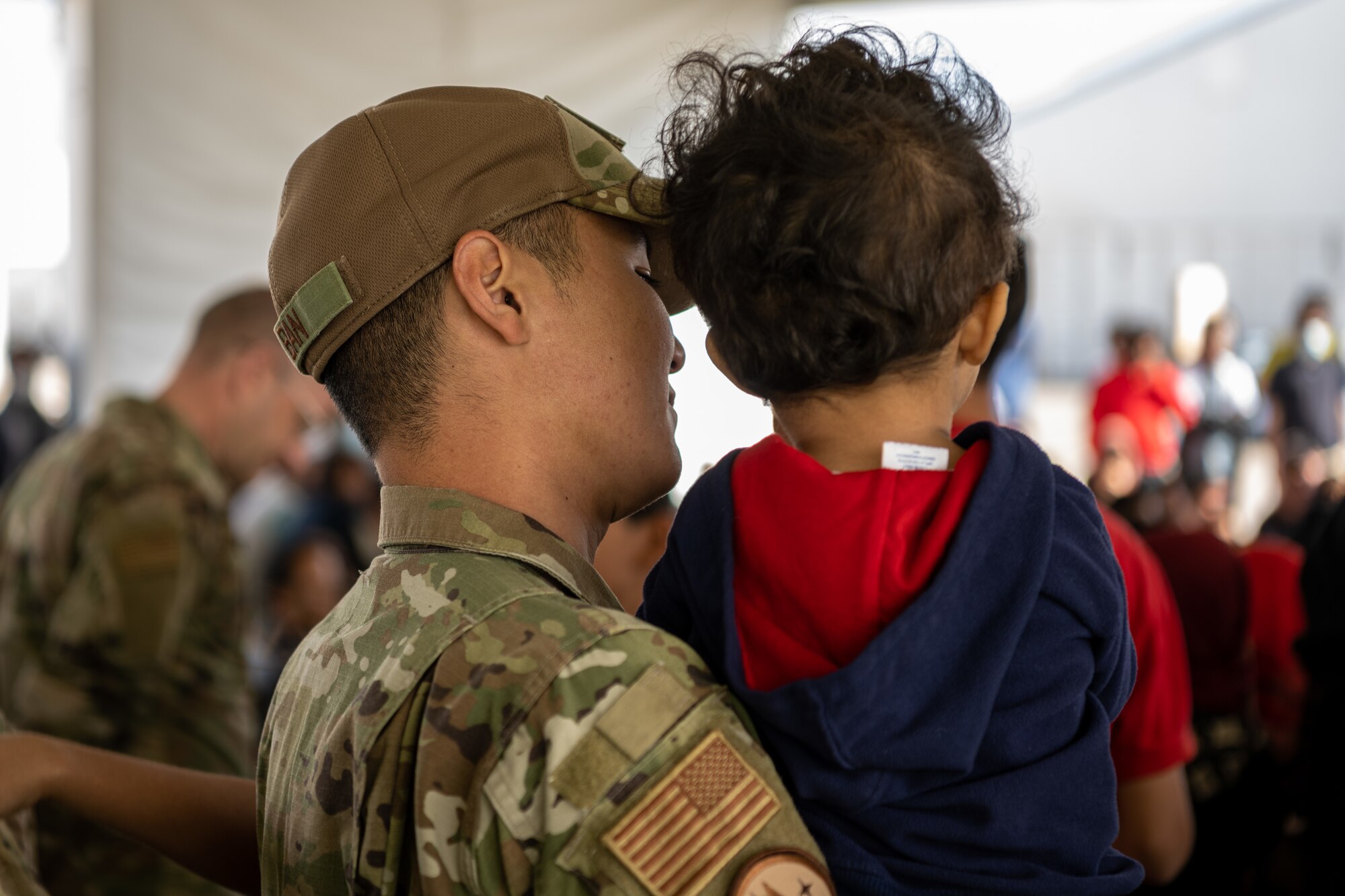 A Task Force-Holloman Airman holds an Afghan child during a performance by the U.S. Air Force Academy Winds musical ensemble at Aman Omid Village on Holloman Air Force Base, New Mexico,  Oct. 12, 2021. The Department of Defense, through U.S. Northern Command, and in support of the Department of Homeland Security is providing transportation, temporary housing, medical screening, and general support for at least 50,000 Afghans at suitable facilities, in permanent or temporary structures, as quickly as possible. This initiative provides Afghan personnel essential support at secure locations outside Afghanistan. (U.S. Air Force photo by Senior Airman Skyler Combs)