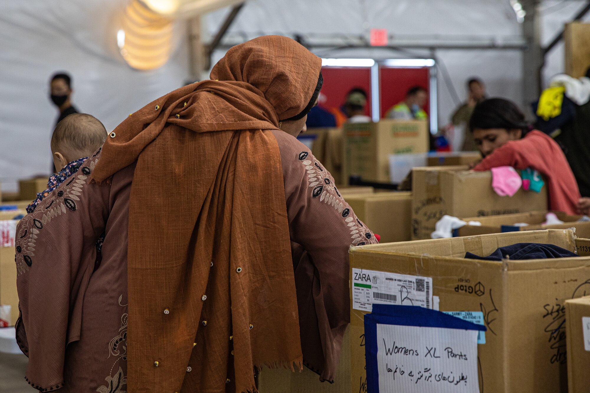 Afghan evacuees sort through donations at the donation center at Task Force-Holloman on Holloman Air Force Base, New Mexico, Oct. 9, 2021. The Department of Defense, through U.S. Northern Command, and in support of the Department of Homeland Security, is providing transportation, temporary housing, medical screening, and general support for at least 50,000 Afghan evacuees at suitable facilities, in permanent or temporary structures, as quickly as possible. This initiative provides Afghan personnel essential support at secure locations outside Afghanistan. (U.S. Army photo by Pfc. Anthony Sanchez)