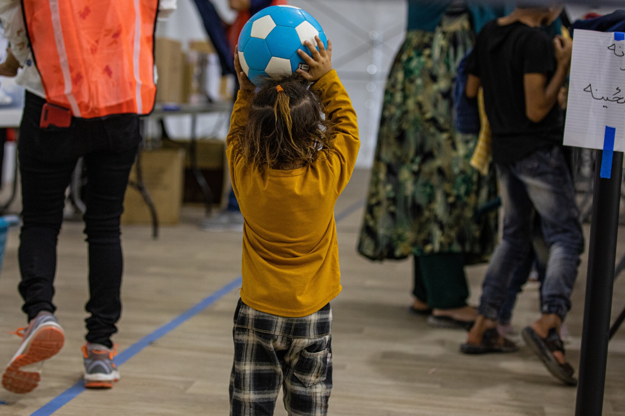 An Afghan child plays with a ball while her family waits in line at the donation center at Task Force-Holloman on Holloman Air Force Base, New Mexico, Oct. 9, 2021. The Department of Defense, through U.S. Northern Command, and in support of the Department of Homeland Security, is providing transportation, temporary housing, medical screening, and general support for at least 50,000 Afghan evacuees at suitable facilities, in permanent or temporary structures, as quickly as possible. This initiative provides Afghan personnel essential support at secure locations outside Afghanistan. (U.S. Army photo by Spc. Nicholas Goodman)