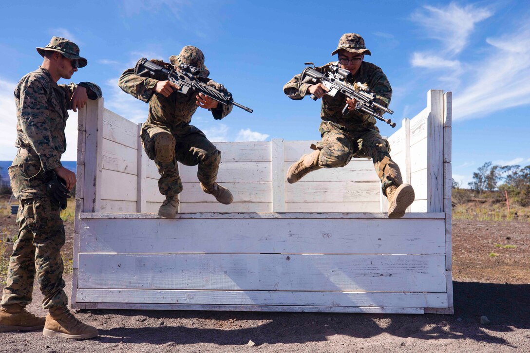 Two Marines jump from a platform as another Marine watches.