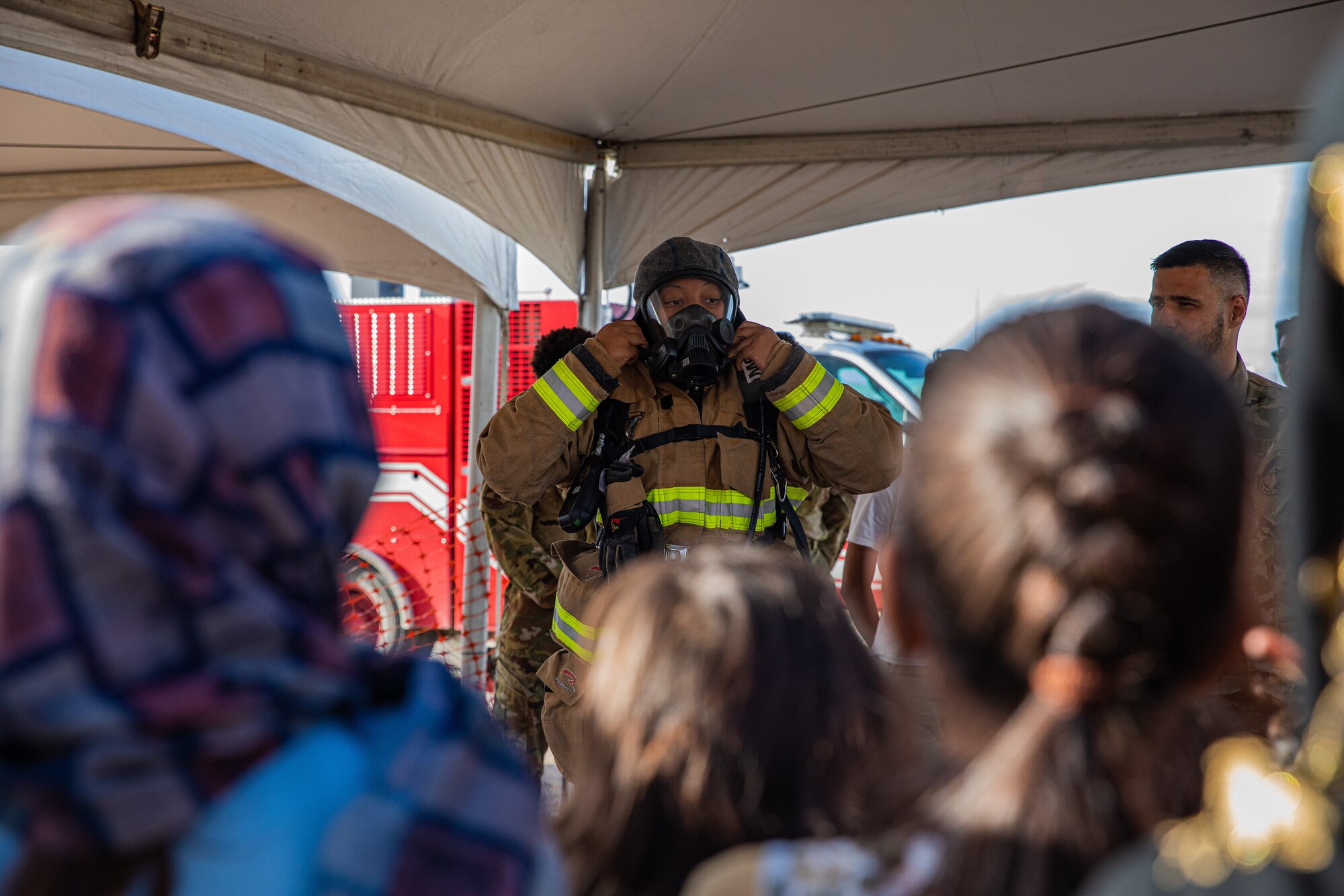 Airman 1st Class Justice Smith, Task Force-Holloman firefighter deployed from Seymour Johnson Air Force Base, North Carolina, demonstrates the proper wear of firefighter gear as well as giving a fire safety class to younger Afghan evacuees on Holloman Air Force Base, New Mexico, Oct. 11, 2021. The Department of Defense, through U.S. Northern Command, and in support of the Department of Homeland Security, is providing transportation, temporary housing, medical screening, and general support for at least 50,000 Afghan evacuees at suitable facilities, in permanent or temporary structures, as quickly as possible. This initiative provides Afghan personnel essential support at secure locations outside Afghanistan. (U.S. Army photo by Pfc. Anthony Sanchez)
