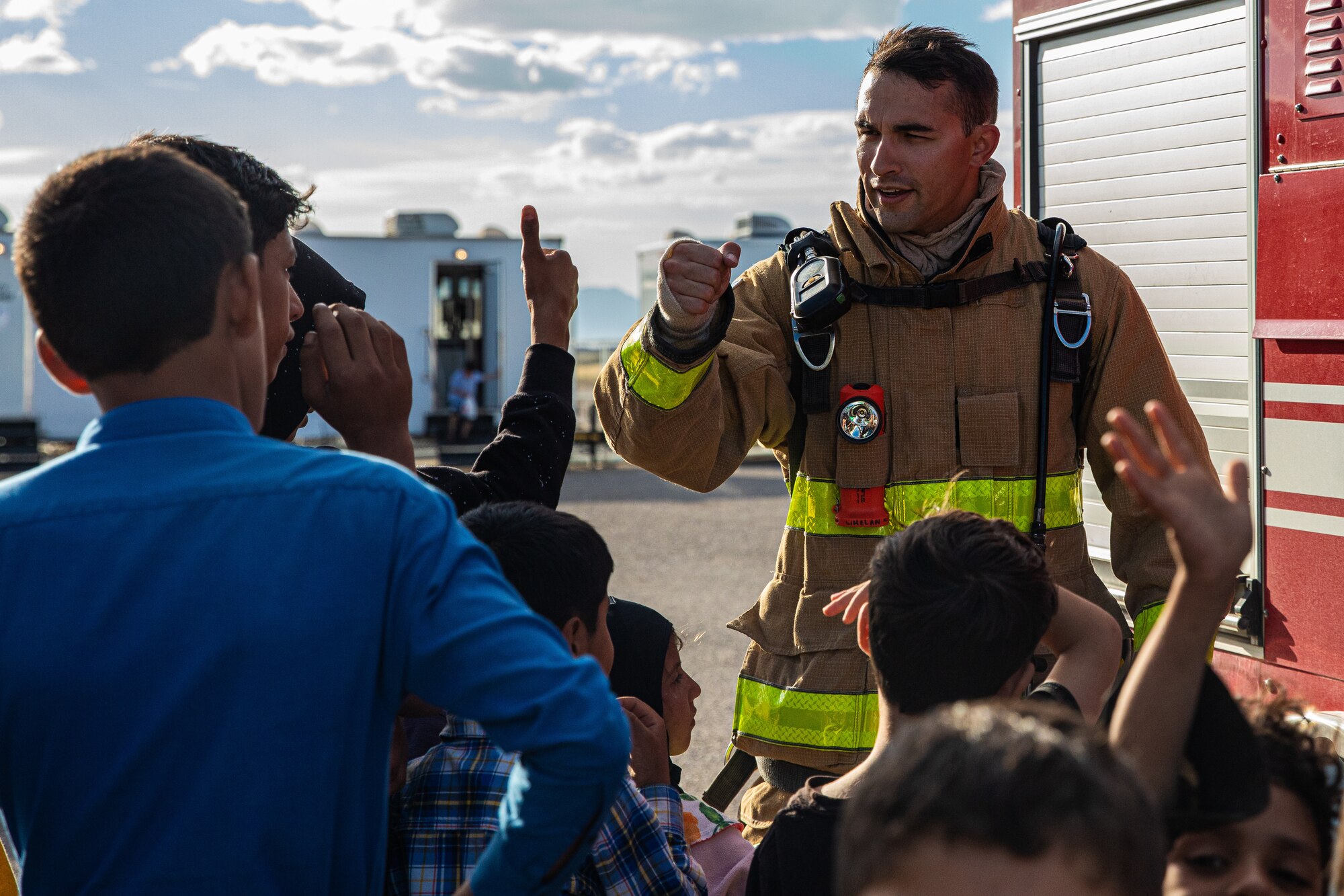 Tech. Sgt. Matt Whelan, Task Force-Holloman firefighter deployed from Seymour Johnson Air Force Base, North Carolina, gives a fist bump to Afghan children during a fire safety class at Aman Omid Village on Holloman Air Force Base, New Mexico, Oct. 11, 2021. The Department of Defense, through U.S. Northern Command, and in support of the Department of Homeland Security, is providing transportation, temporary housing, medical screening, and general support for at least 50,000 Afghan evacuees at suitable facilities, in permanent or temporary structures, as quickly as possible. This initiative provides Afghan personnel essential support at secure locations outside Afghanistan. (U.S. Army photo by Pfc. Anthony Sanchez)
