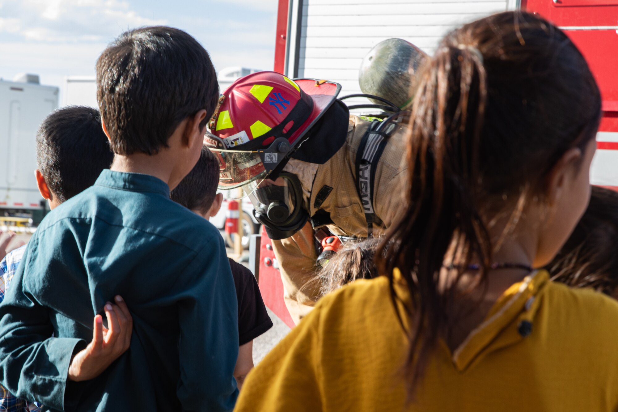 A Task Force-Holloman firefighter speaks with Afghan children at the end of a fire safety class given to young Afghan evacuees on Holloman Air Force Base, New Mexico, Oct. 11, 2021. The Department of Defense, through the U.S. Northern Command, and in support of the Department of State and Department of Homeland Security, is providing transportation, temporary housing, medical screening, and general support for at least 50,000 Afghan evacuees at suitable facilities, in permanent or temporary structures, as quickly as possible. This initiative provides Afghan evacuees essential support at secure locations outside Afghanistan. (U.S. Army photo by Spc. Nicholas Goodman)
