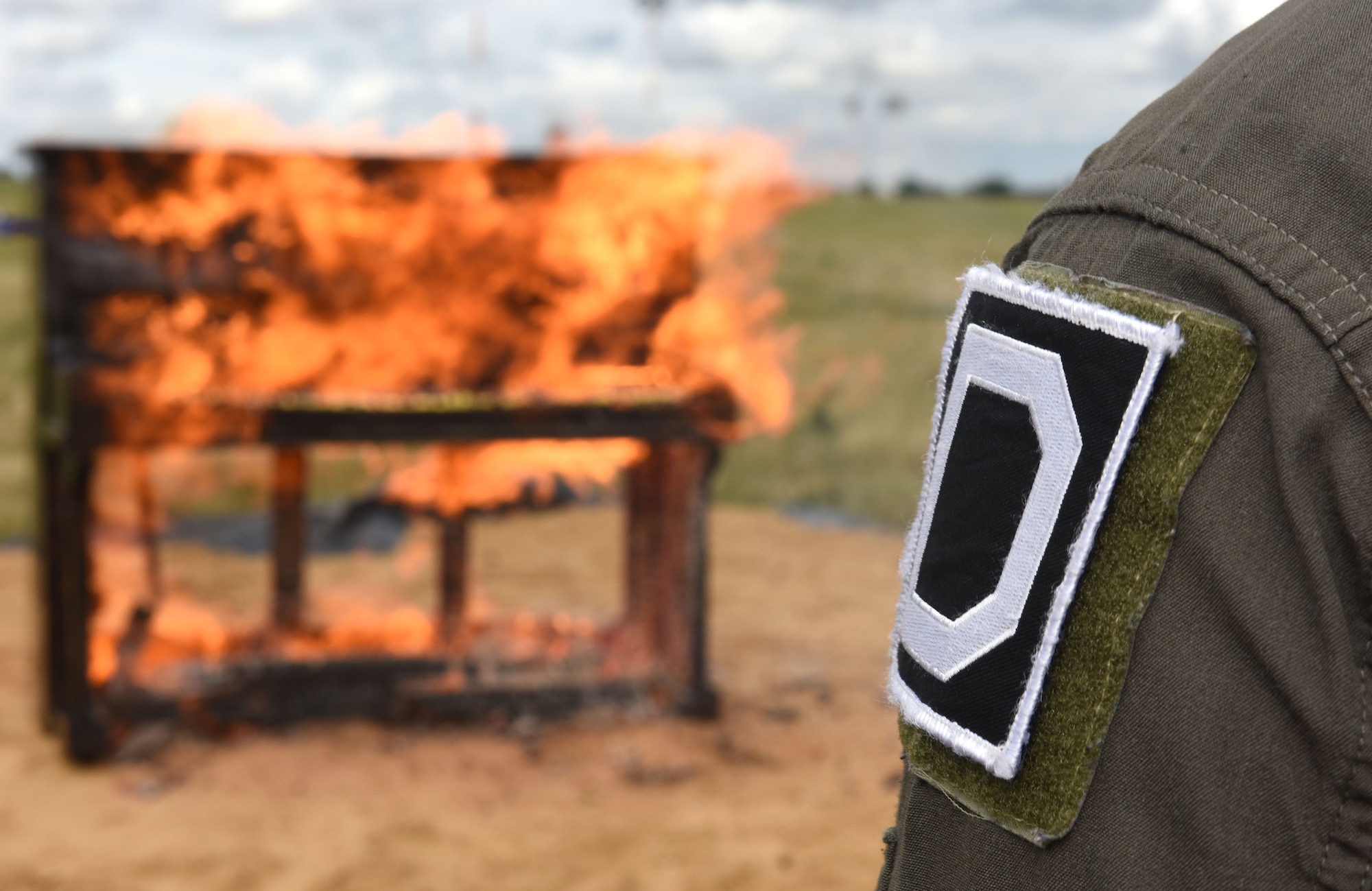 A pilot in the 100th Operations Group displays the Square D patch on his shoulder as he watches a piano burn at Royal Air Force Mildenhall, England Oct. 1, 2021. The 100th OG set fire to the piano as they followed an RAF World War II tradition to remember U.S. service members who paid the ultimate sacrifice as a result of a bomb attack at Kabul airport in Afghanistan. The event also marked the end of a successful flying and fiscal year for 2021, and the team’s hard work in Rockin’ ‘D’ Mish. (U.S. Air Force photo by Karen Abeyasekere)