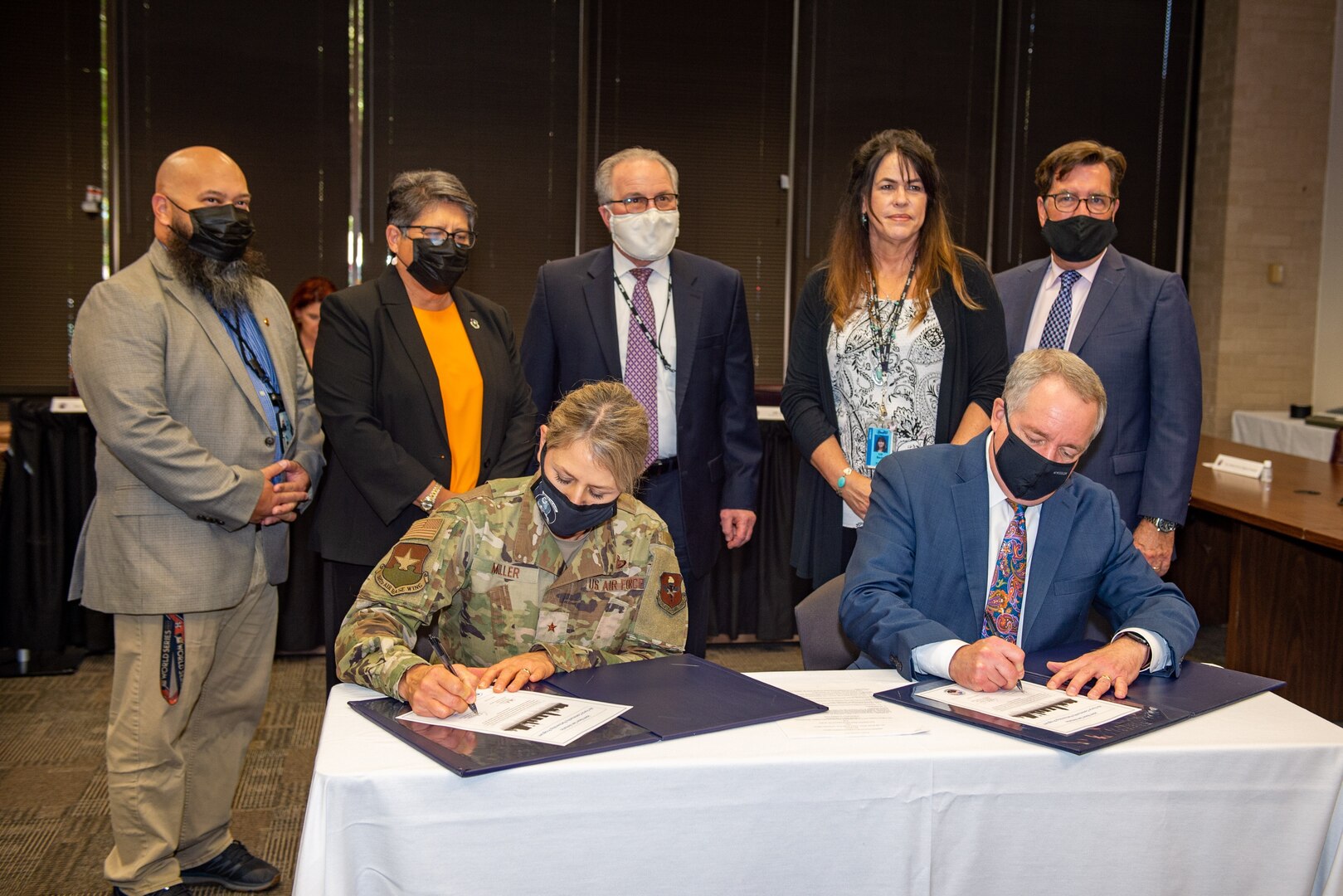 Two individuals signing documents, with five individuals standing behind.