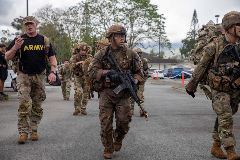 Soldiers carrying weapons and full backpacks walk along a road.