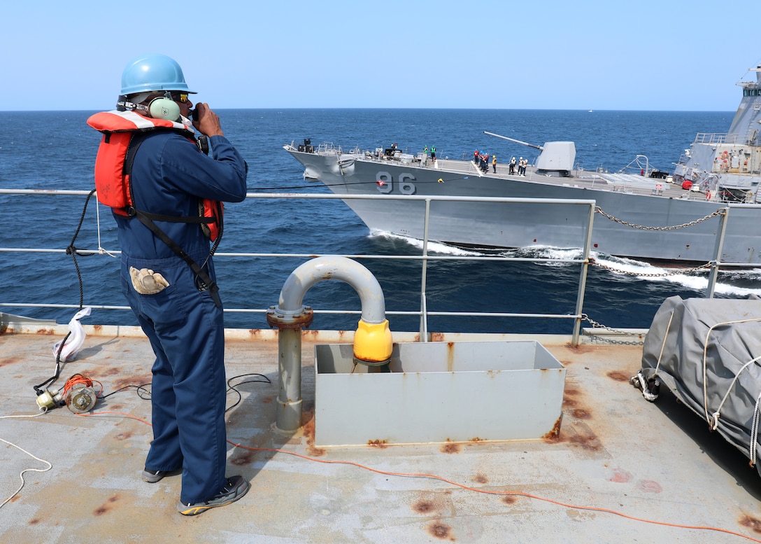 A civilian mariner speaks to the crew of a Navy destroyer during an at-sea resupply.