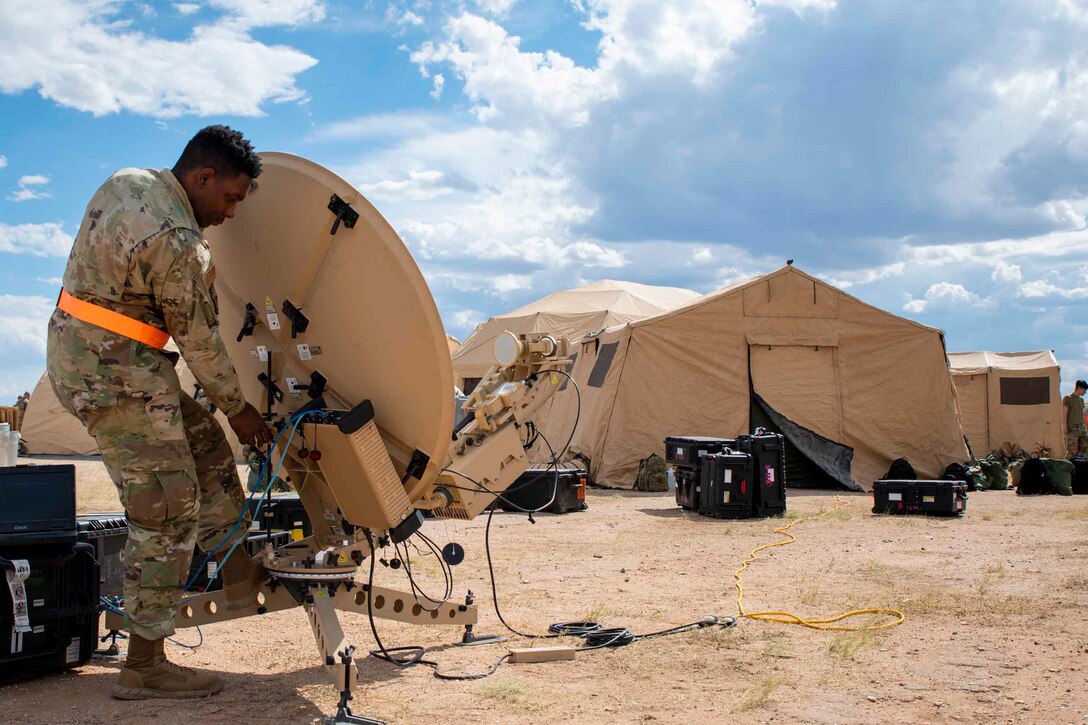 An airman sets up a satellite at a campsite.