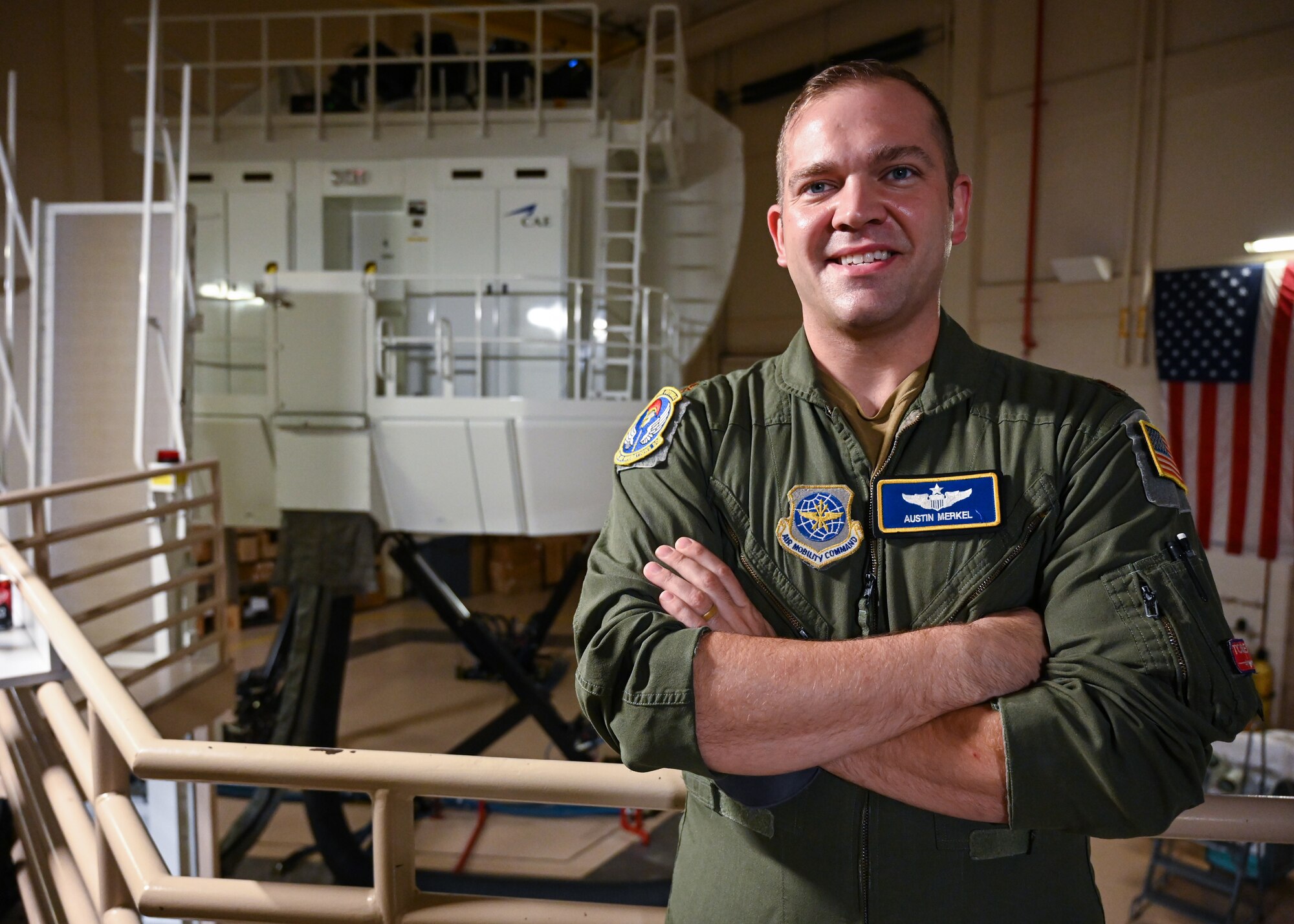 An Airman stands in front of a C-130J Super Hercules simulator.