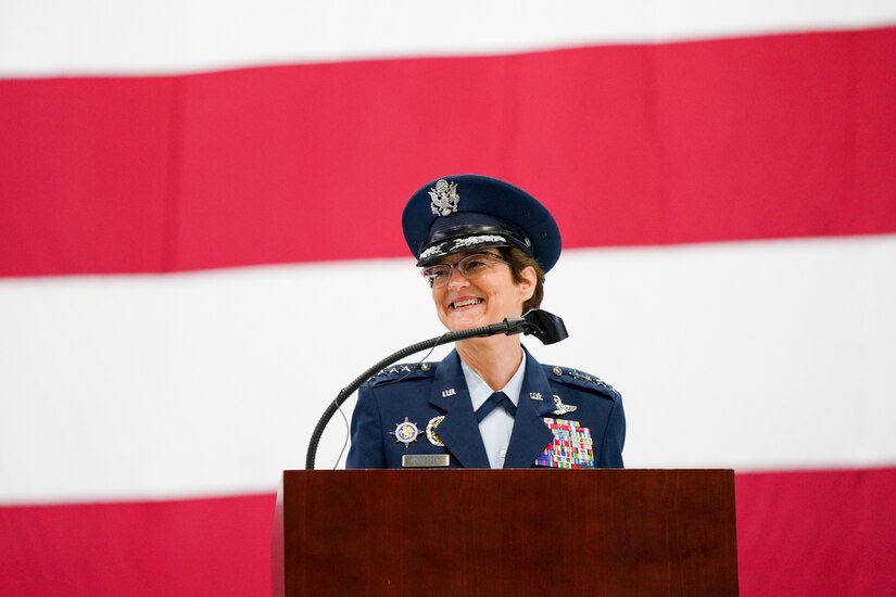 An Air Force general speaks at a lectern in front of a large American flag.
