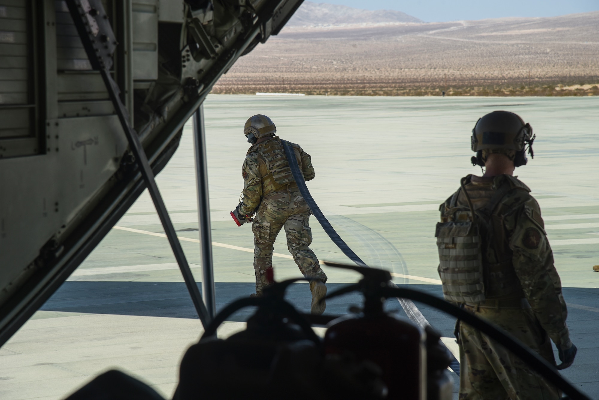 Pictured above are two Airmen, one Airman runs with a hose while the other waits on standby.