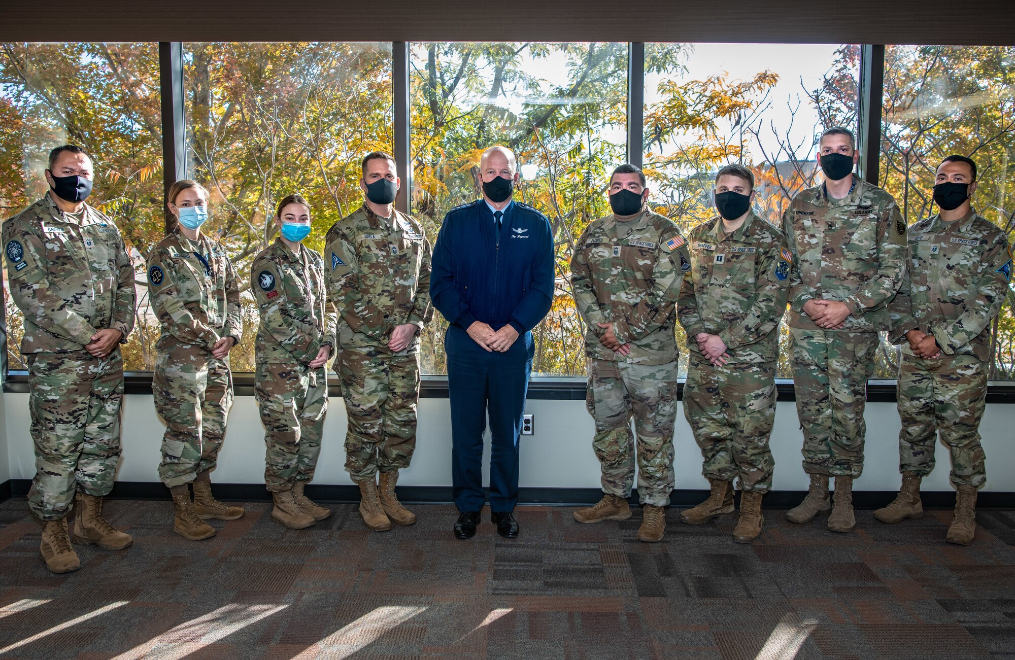 General Raymond poses with guardians in front of a window at the dining facility on schriever space force base.