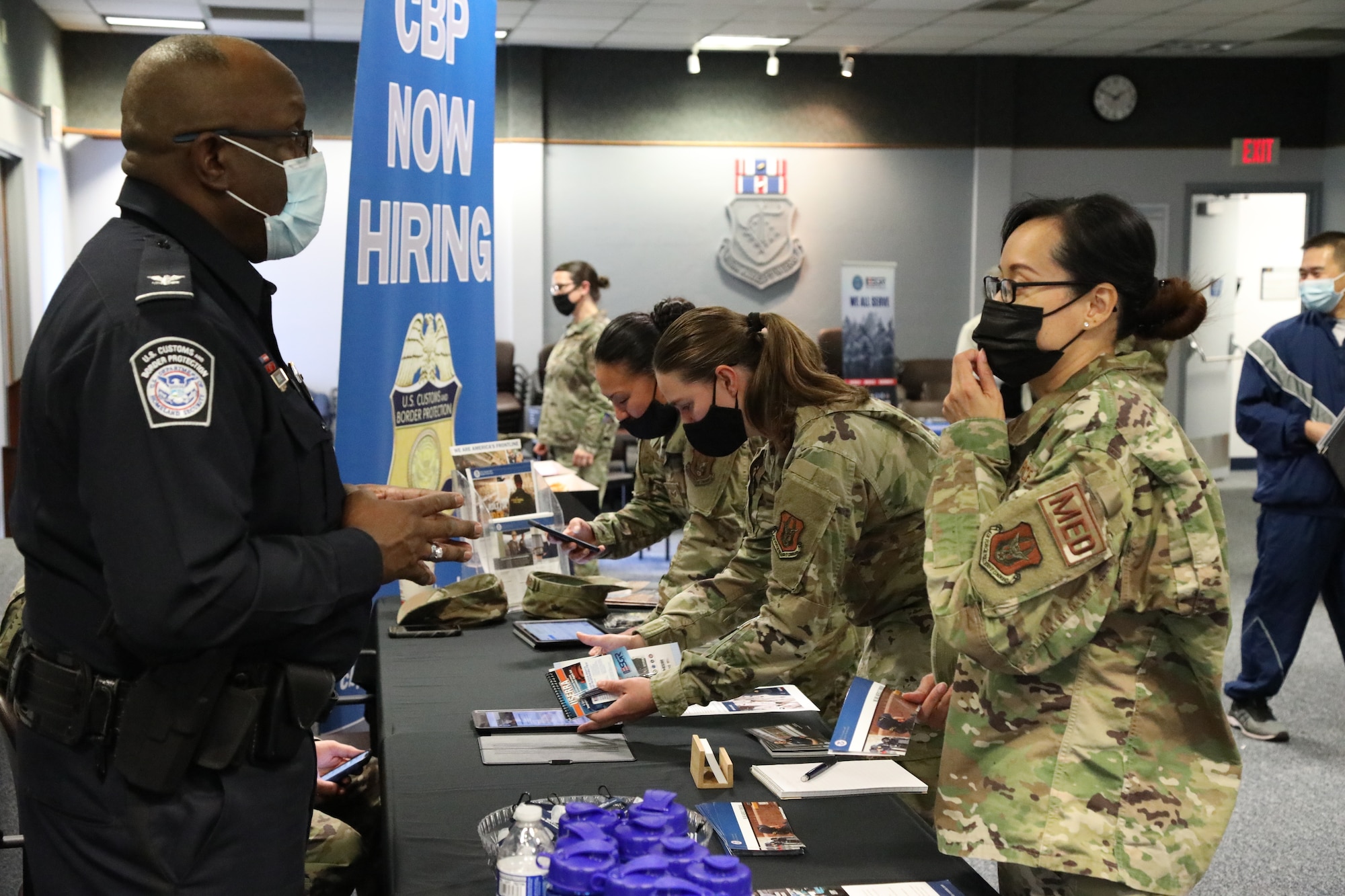 Female Airmen talk to Customs and Border Protection recruiter at a booth.