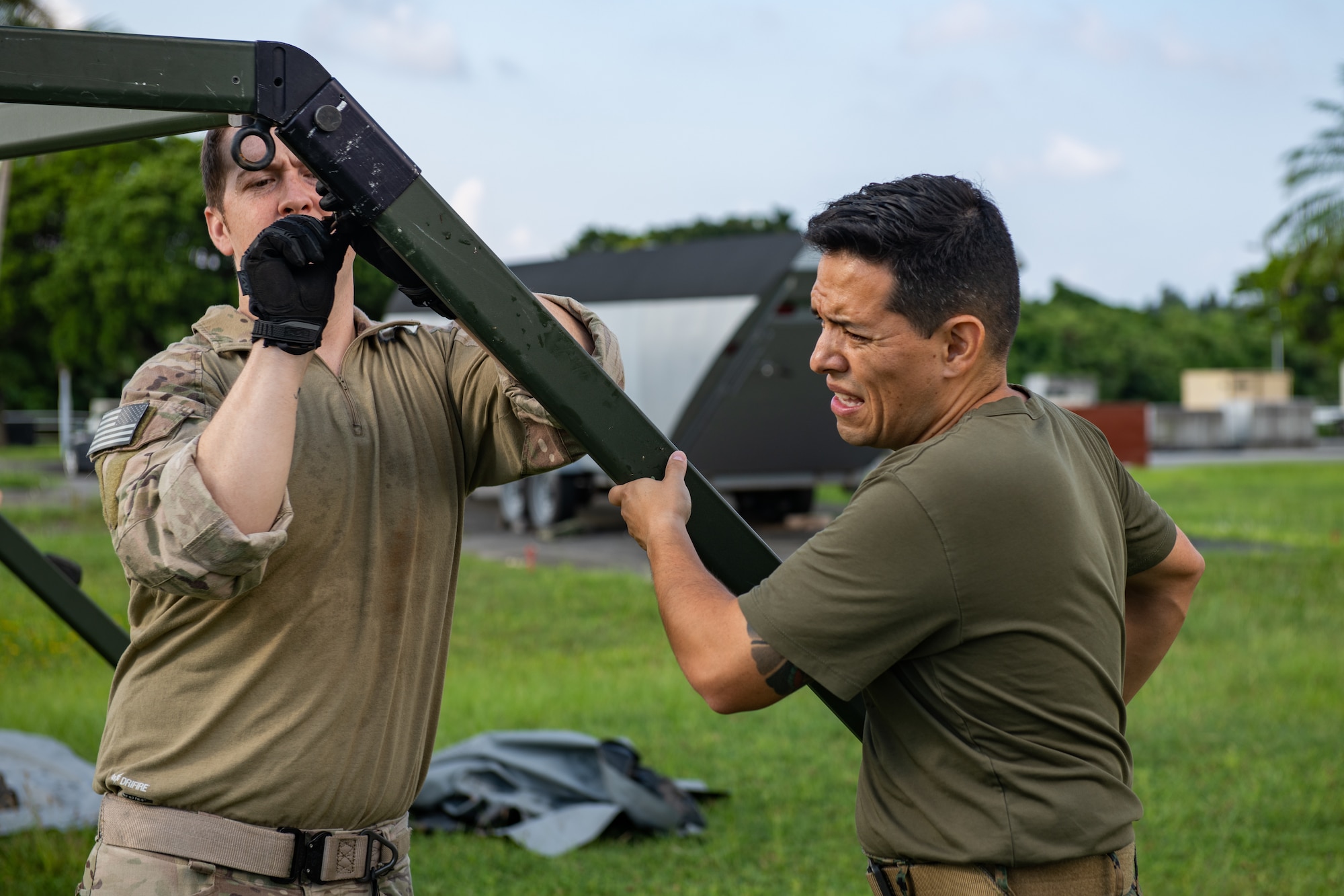 Two military members hold up the leg of a tent