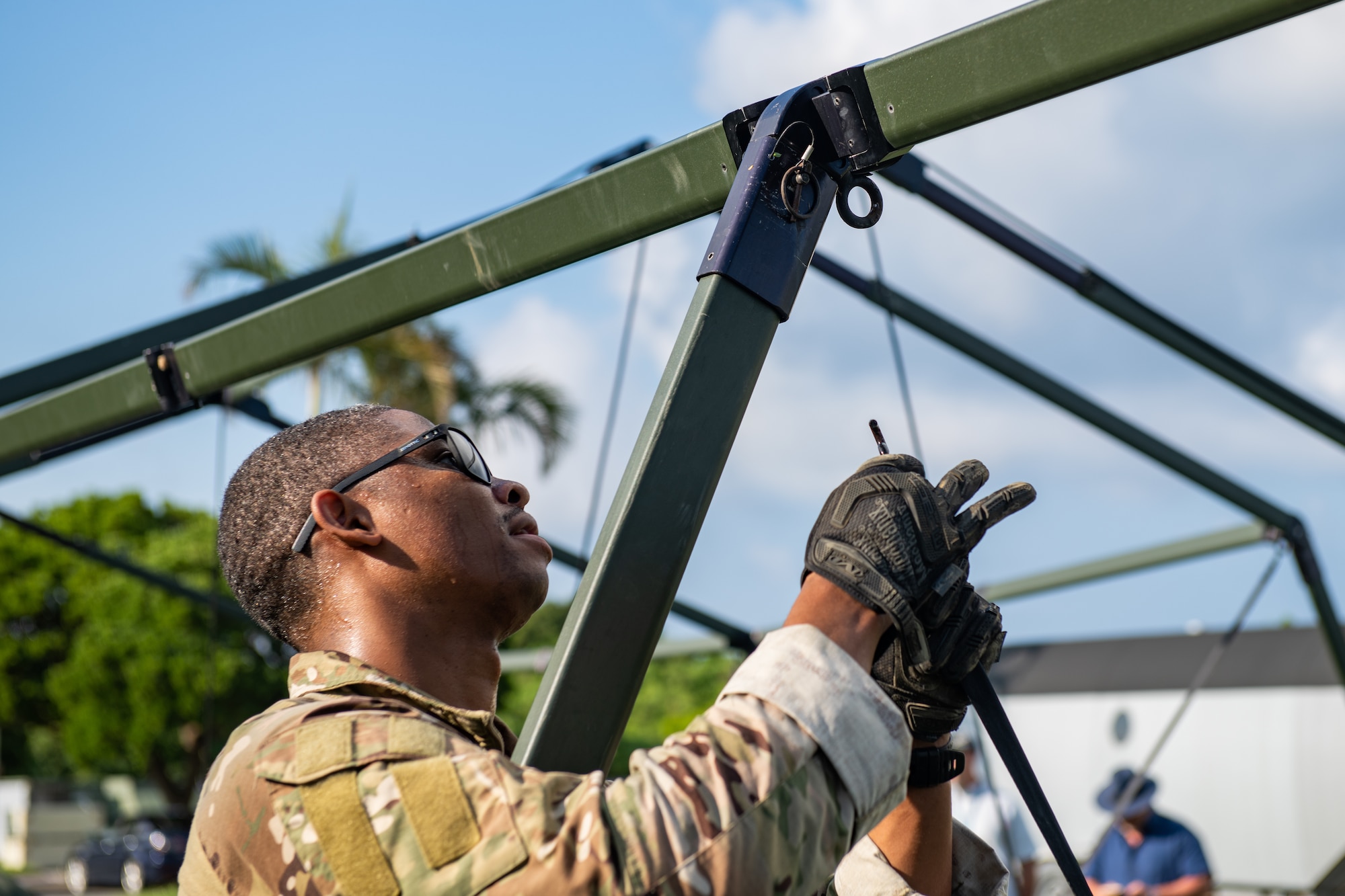 A man holds a pin up to a joint of one of the frame legs for a big tent