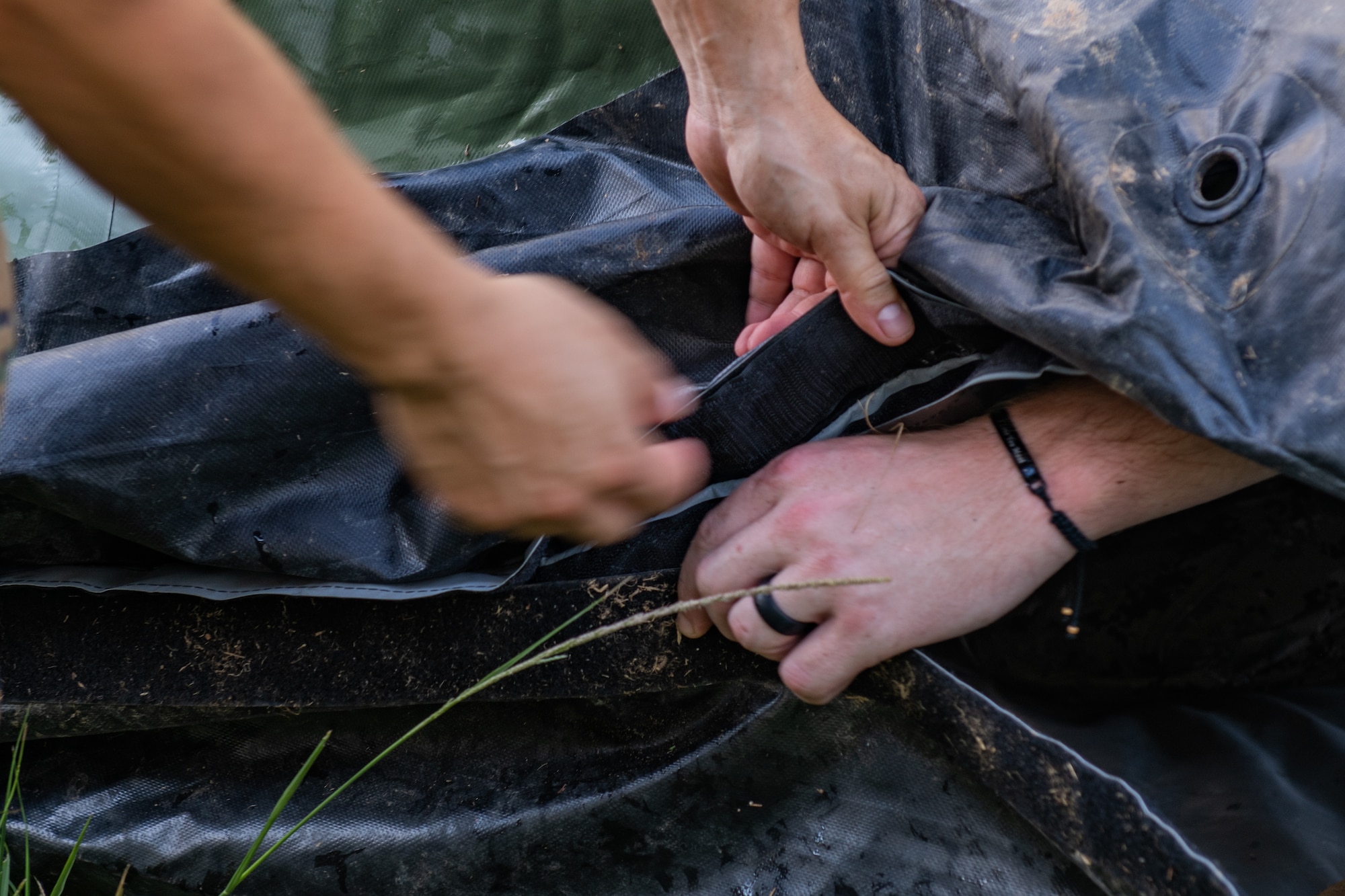 The hands of some military personnel work together to put floor flaps together of a tent