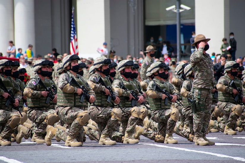 Foreign troops hold weapons across their chests as they kneel on one knee.