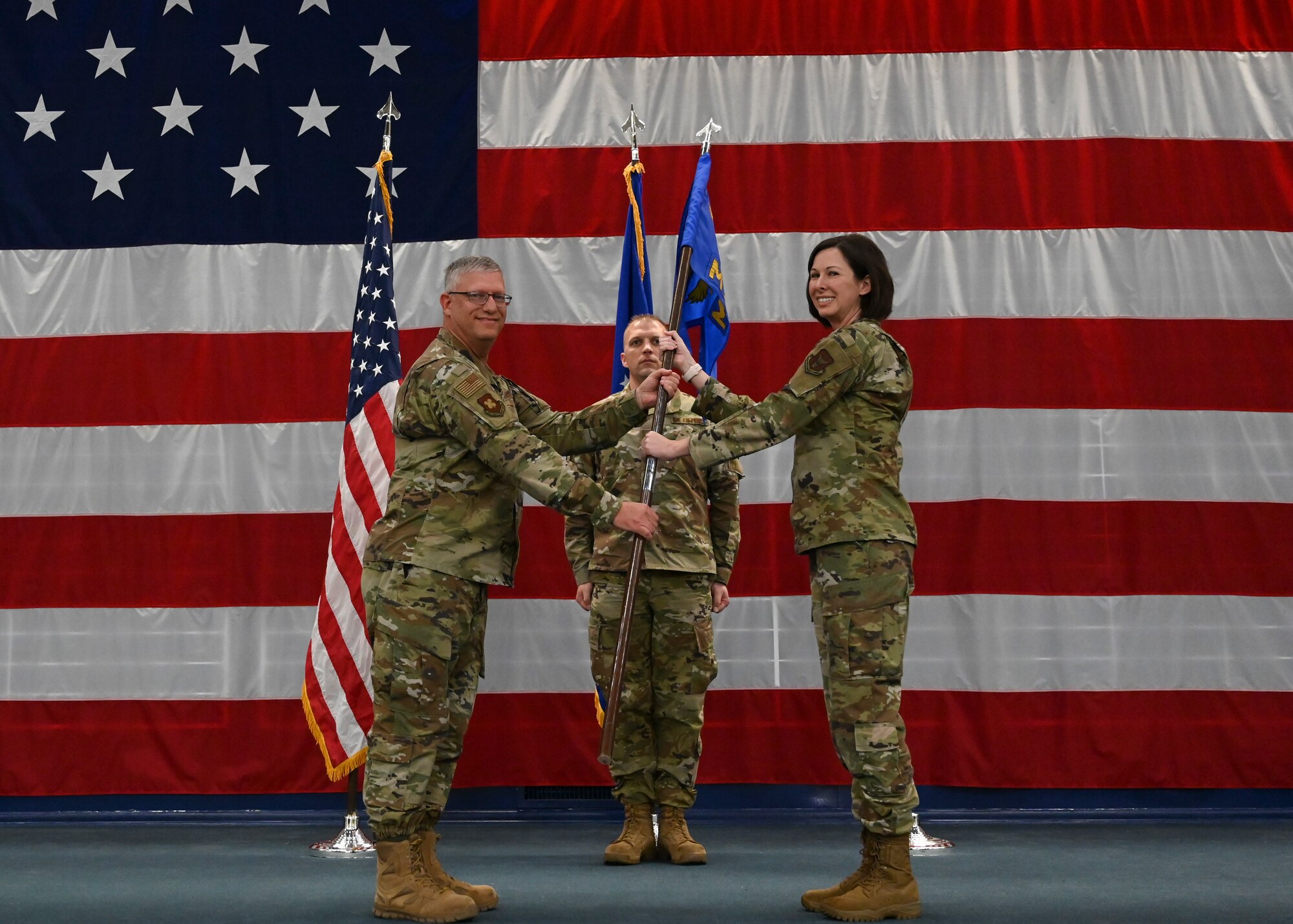 Three U.S. Airmen stand in front of a large U.S. flag