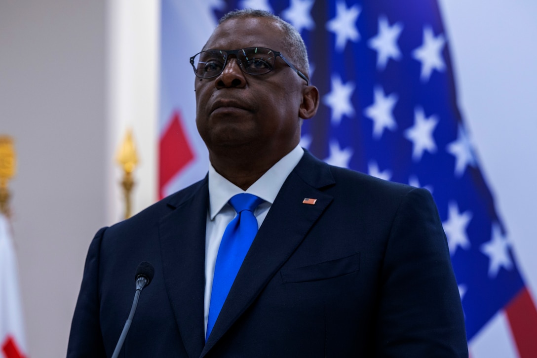 Defense Secretary Lloyd J. Austin III stands at a microphone in front of an American flag.