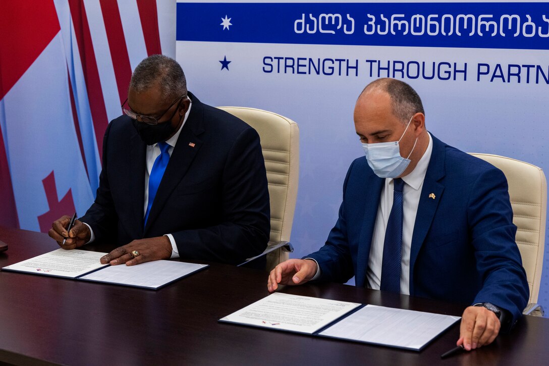 Two men sit at a table signing papers.