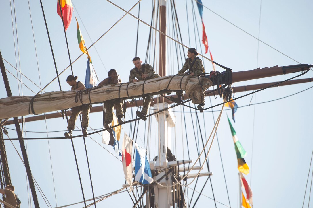 Four sailors work on a ships top sail.