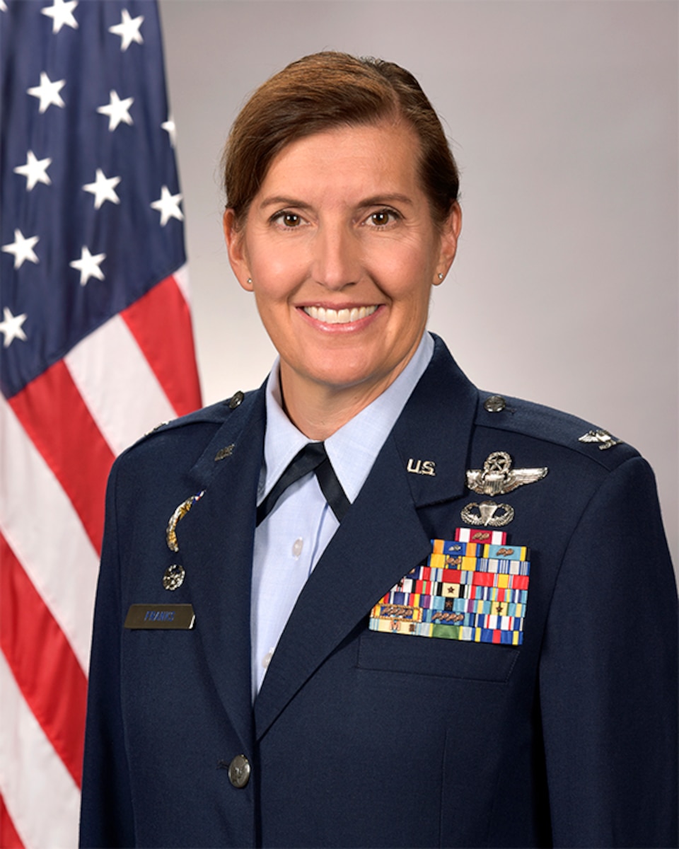 Studio photo of a woman with a Col. rank adorned in Air Force service dress in front of an American flag.