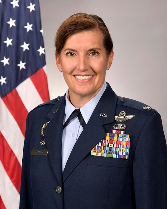 Studio photo of a woman with a Col. rank adorned in Air Force service dress in front of an American flag.