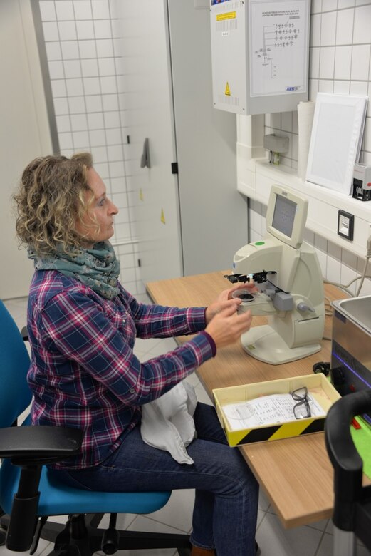 Yvonne Gortner, right, prescription eyeglass maker supervisor for USAMMCE works with Col. Shane Roach, USAMMC-E commander, to grind a new pair of custom eyeglasses. The digitally controlled equipment grinds a lens from a blank lens to create custom lenses for non-typical prescriptions.