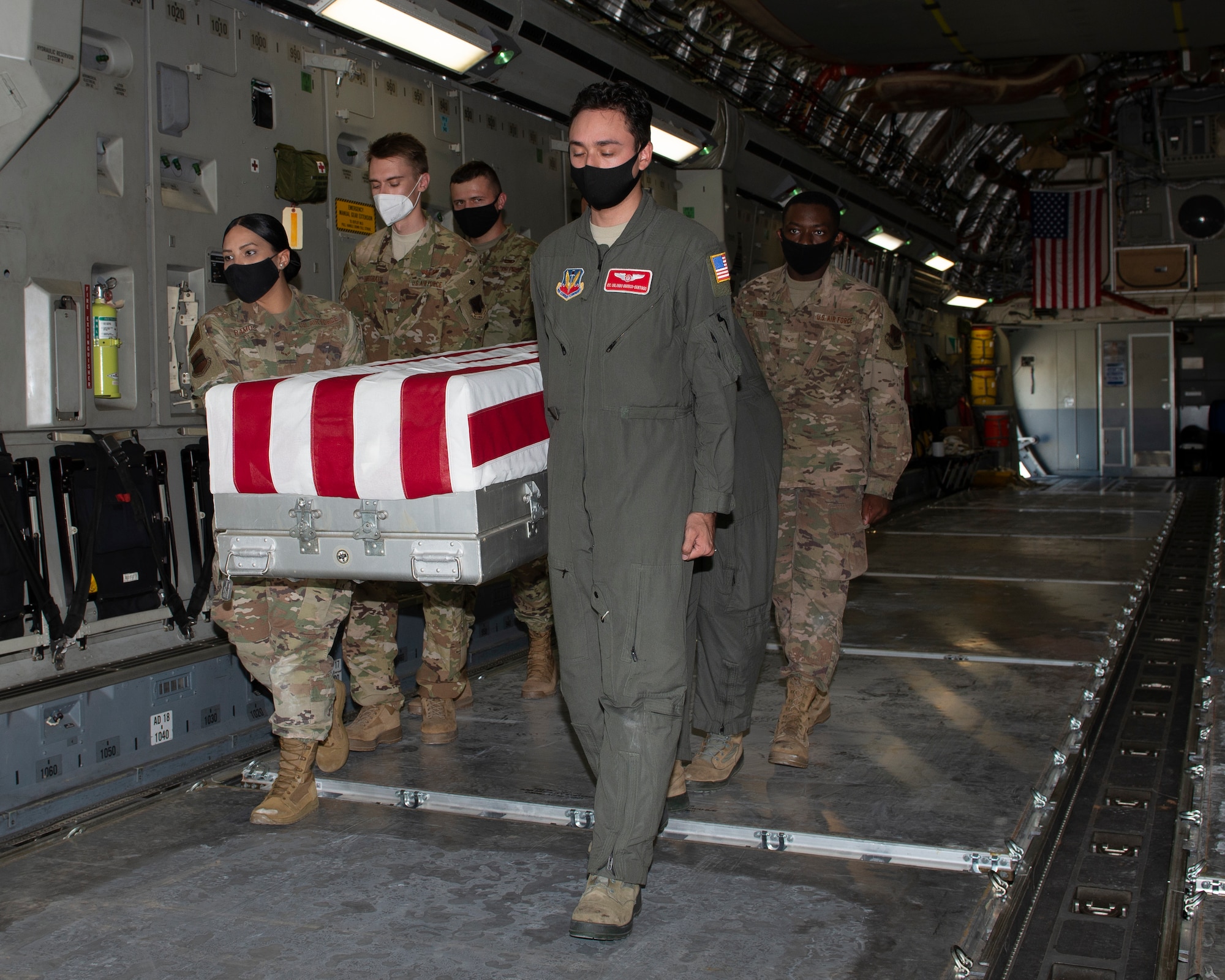 Six Air Force service members carry a casket draped with an American flag off a military airplane.