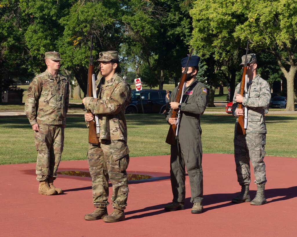 Three Airmen hold rifles and stand ready in formation while another Airmen gives orders.