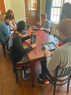 Students sit around a table using touchscreen devices.