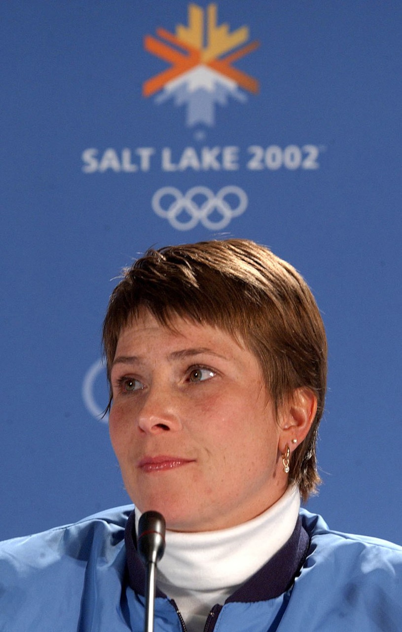 Woman at a microphone looks off into the distance. A sign in the background indicates that she is at the 2002 Winter Olympics in Salt Lake City.