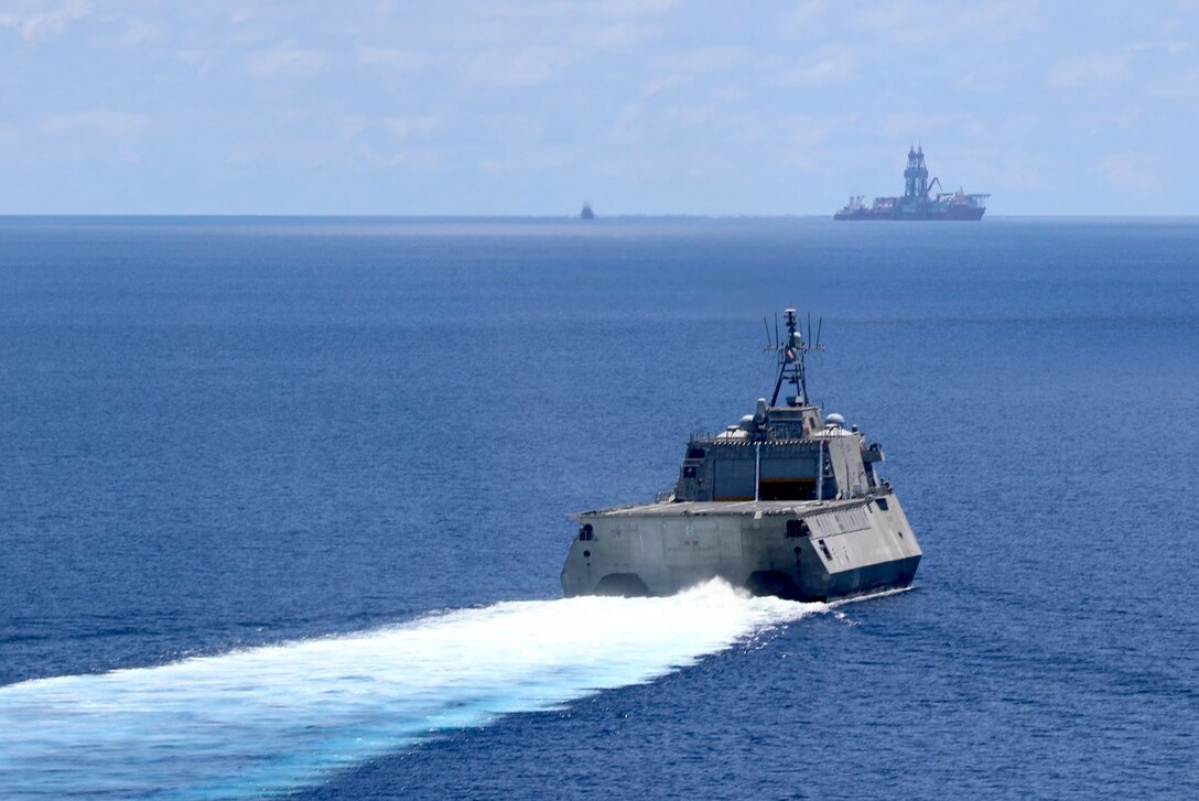 A combat ship sails toward a drill ship.
