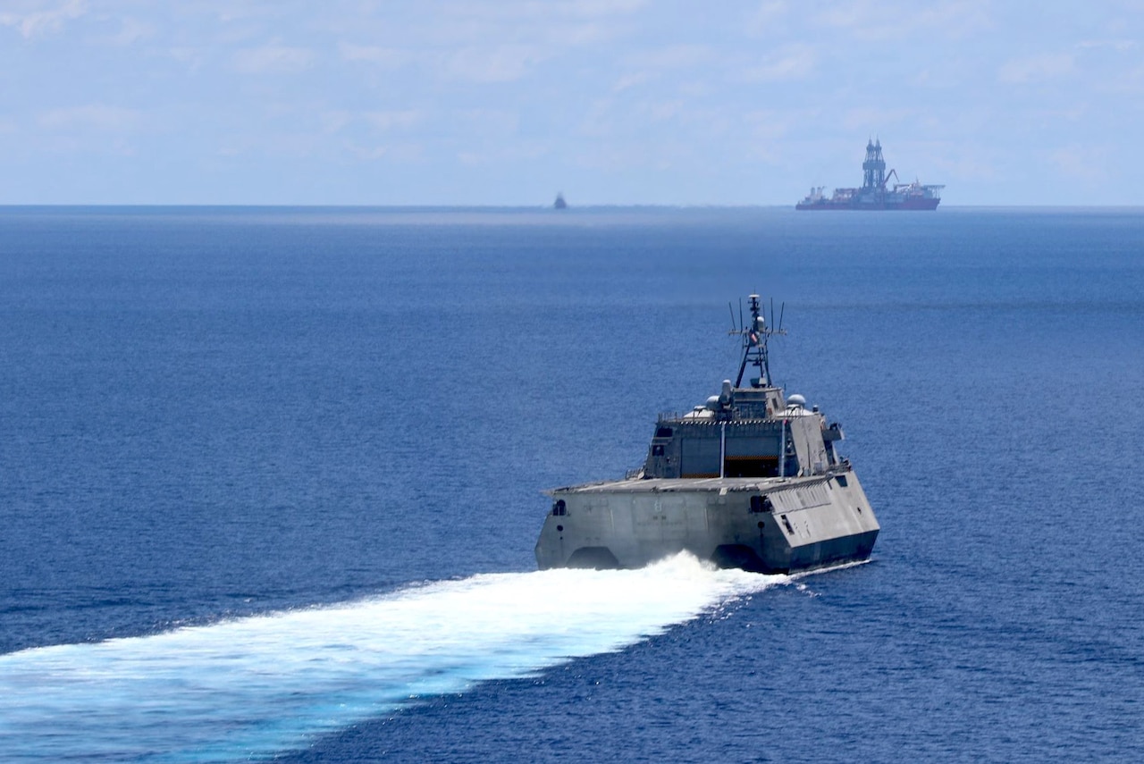 A combat ship sails toward a drill ship.