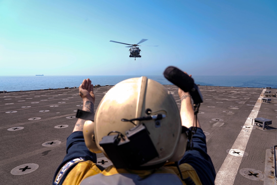 A sailor signals to a helicopter preparing to land on a ship at sea.