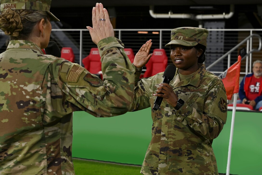 Airmen face each other while holding up their right hands on a soccer field.
