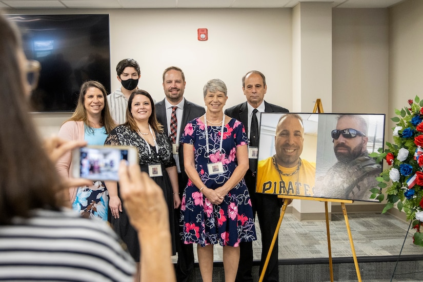A family friend of Michael G. Sauro, a former Defense Ammunition Center hazardous material instructor who lost his life while deployed as a civilian in support of Operation Freedom’s Sentinel, takes a photo of Sauro’s immediate family members during a building dedication ceremony at Camp Atterbury, Ind., June 3, 2021. Pictured from left to right are Brienne Matthews, sister; William Matthews, nephew; Sarah Sauro, sister-in-law; Ben Sauro, brother; Christine Sauro, mother; and Michel E. Sauro, father. (U.S. Army photo by Mark R. W Orders-Woempner)