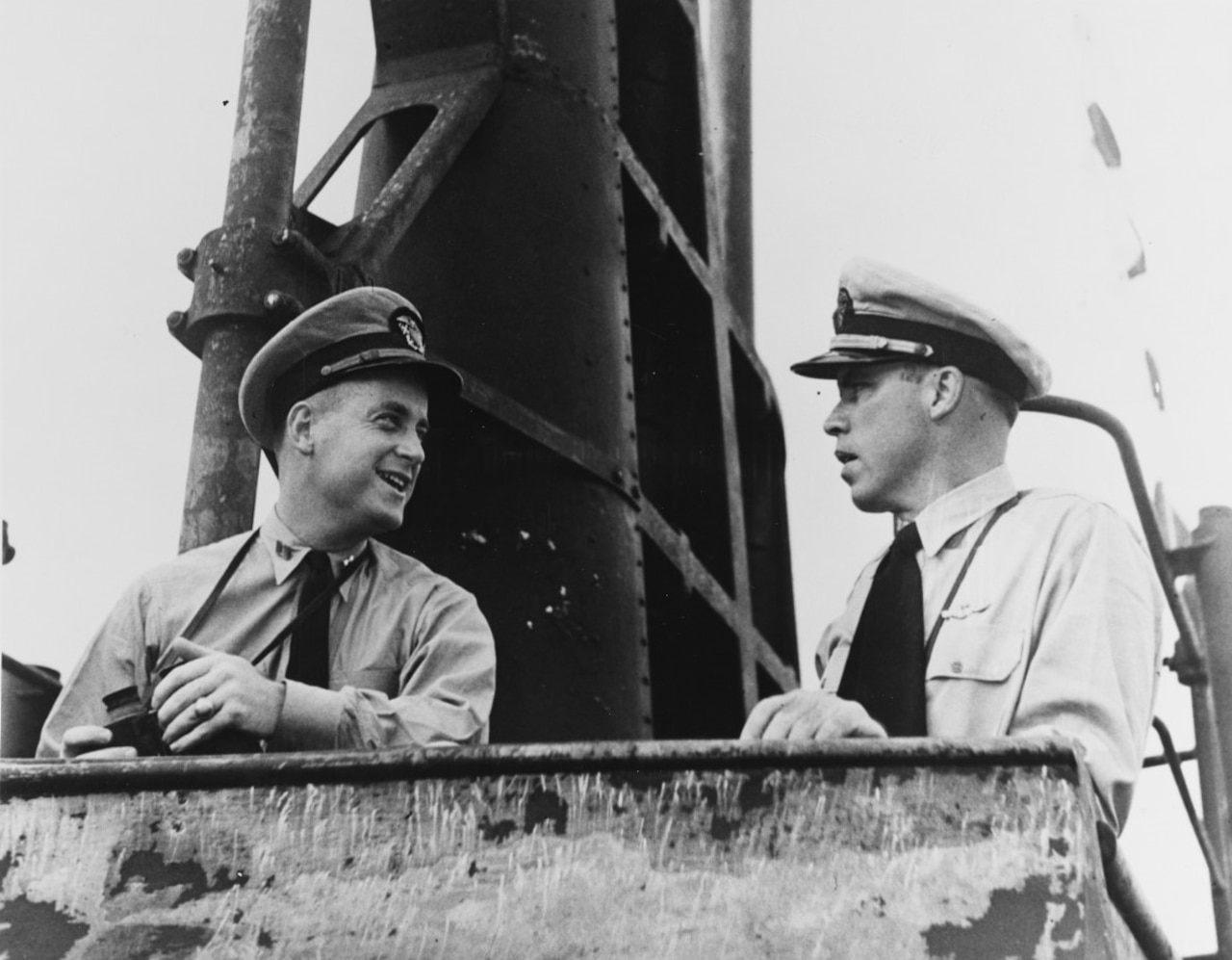 Two men in sailor caps stand with their arms resting on a metal ledge.