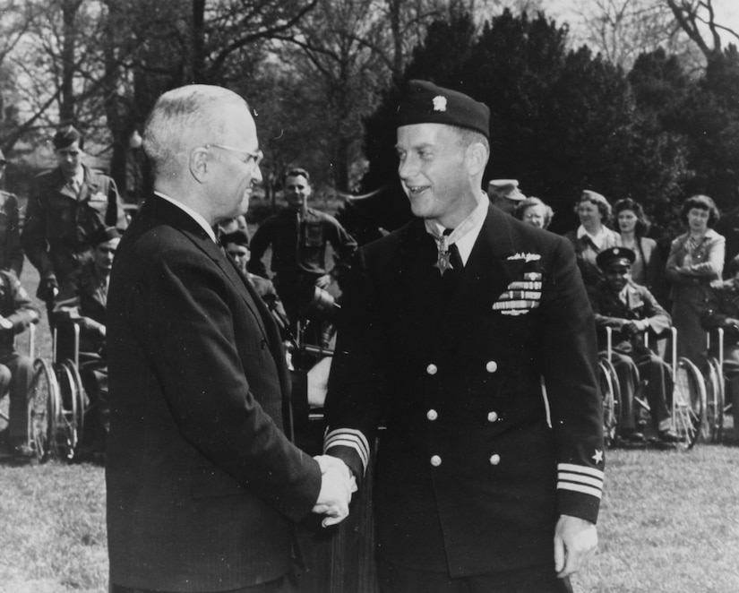 Two men shake hands. Several others look toward them in the background.